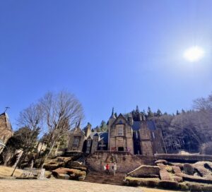 青空の下、太陽の光を浴びてそびえ立つ群馬県高山村のロックハート城。中世スコットランドから移築された石造りの古城と、階段を上がる来場者の様子。