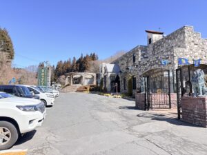 ロックハート城の駐車場とエントランス。石造りの門柱に設置されたライオンの石像と、立ち並ぶ車、青空の下の洋風な建物。