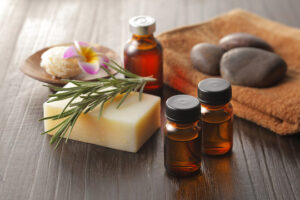 木のテーブルに並んだアロマオイルの小瓶と、フレッシュなローズマリー、ハーブ石鹸。