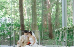 群馬県高山村・ロックハート城の豊かな森に包まれた結婚式。ガラス越しに広がる新緑を背景に、新郎新婦が寄り添う幻想的なロケーションフォトとナチュラルな挙式スタイル。