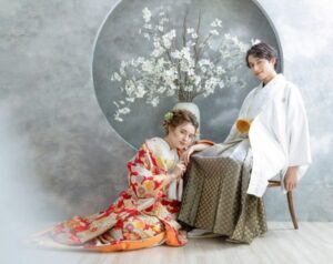 モダンな円窓と白い花が活けられた花瓶を背景に、白無垢の新婦と白の紋付袴を纏った新郎が寄り添う和装ショット。**「スイセン」**の無垢な白が「希望」を象徴するように、清らかで凛とした空気が漂う。花びらの一枚一枚の重なりを、これから二人が重ねるかけがえのない時間に見立てた、ロックハート城での和装フォト。