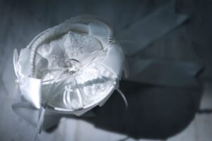 白い刺繍とリボンが施された円形のリングピローに、二つの結婚指輪が結び付けられている。**「アリッサム」**の小さな花たちが手を取り合って咲くように、人生の土台を共に築く決意を象徴。ロックハート城の神聖なチャペル挙式で、主役の指輪を優しく引き立てる謙虚で深い愛の象徴。