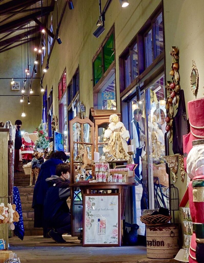 重厚な木の梁が露出したクラシカルな内装のショップ。アンティーク調の小物や猫の人形、クリスマスディスプレイが並び、ランプの温かい光に包まれている。