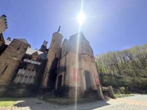 雲一つない青空と強い日差しの下、新緑の森を背景に立つ、石造りのロックハート城の近景。城の入り口には赤い旗とイギリス国旗が掲げられている。