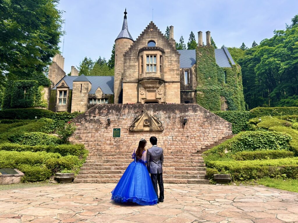 ロックハート城を背景に、青いドレス姿の女性とタキシード姿の男性が並んで立つカップルフォト